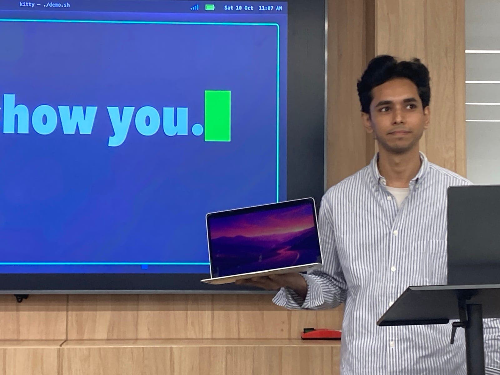 Naeem Malik holding up a MacBook running Omarchy on Apple silicon during his demo at Omarchy New Delhi