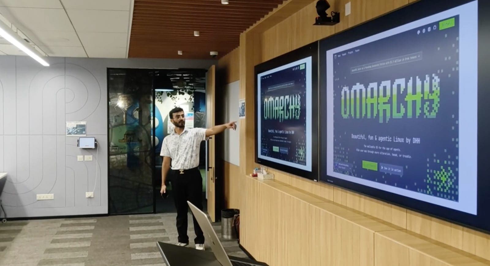 Aryan pointing at the Omarchy homepage on the big screens at Omarchy New Delhi